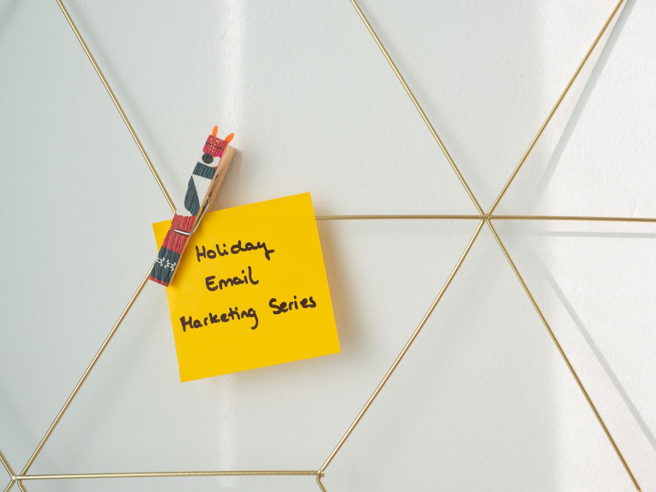 Post-it jaune vif avec un message de marketing par e-mail pour les fêtes, accroché à une grille murale.